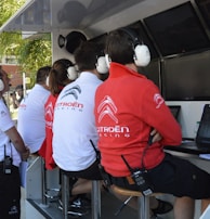 Several people wearing Citroën Racing uniforms and headphones are seated at a technical workstation with laptops and screens. They appear focused on monitoring or analyzing data.