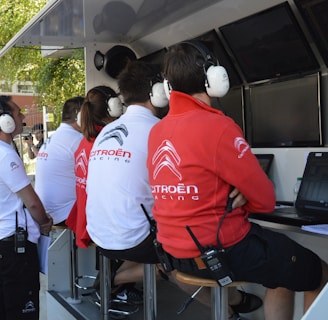 Several people wearing Citroën Racing uniforms and headphones are seated at a technical workstation with laptops and screens. They appear focused on monitoring or analyzing data.