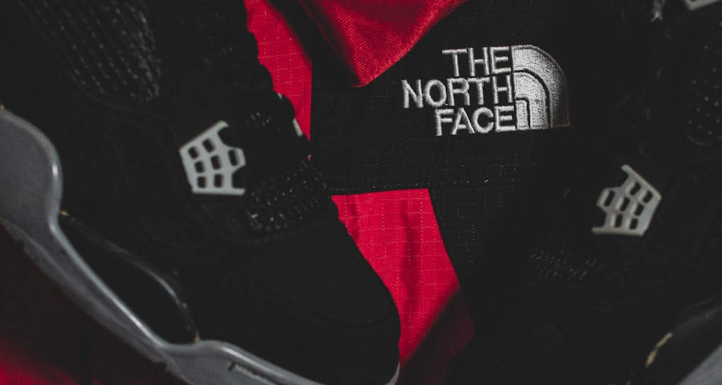 Black athletic shoes are placed alongside red and black sportswear bearing logos from Spalding and The North Face.