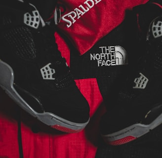 Black athletic shoes are placed alongside red and black sportswear bearing logos from Spalding and The North Face.