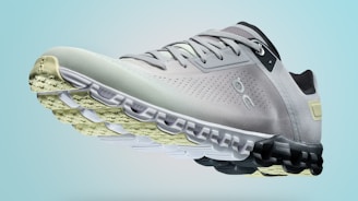 A single sports shoe is prominently displayed against a seamless, light turquoise background. The shoe features a sleek design with a gradient of light gray to dark gray tones, and is equipped with a distinctive CloudTec sole for cushioning. The branding logo is subtly visible on the side.