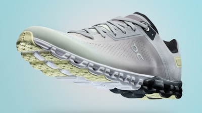 A single sports shoe is prominently displayed against a seamless, light turquoise background. The shoe features a sleek design with a gradient of light gray to dark gray tones, and is equipped with a distinctive CloudTec sole for cushioning. The branding logo is subtly visible on the side.